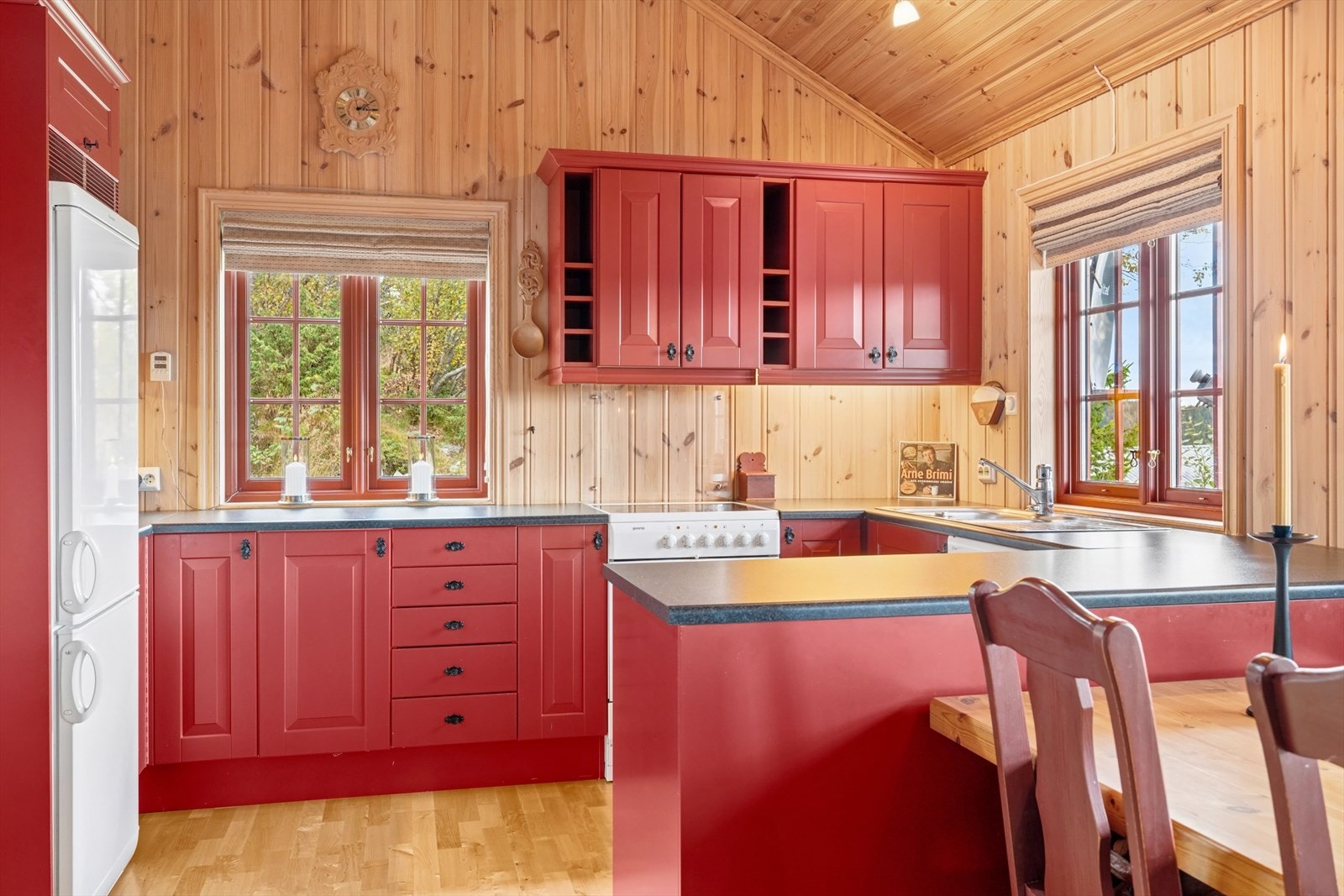 Kjøkkeninnredningen er pen og i tradisjonell hyttestil, med profilerte røde fronter og mørk laminat benkeplate med nedfelt oppvaskkum. Galleribilde