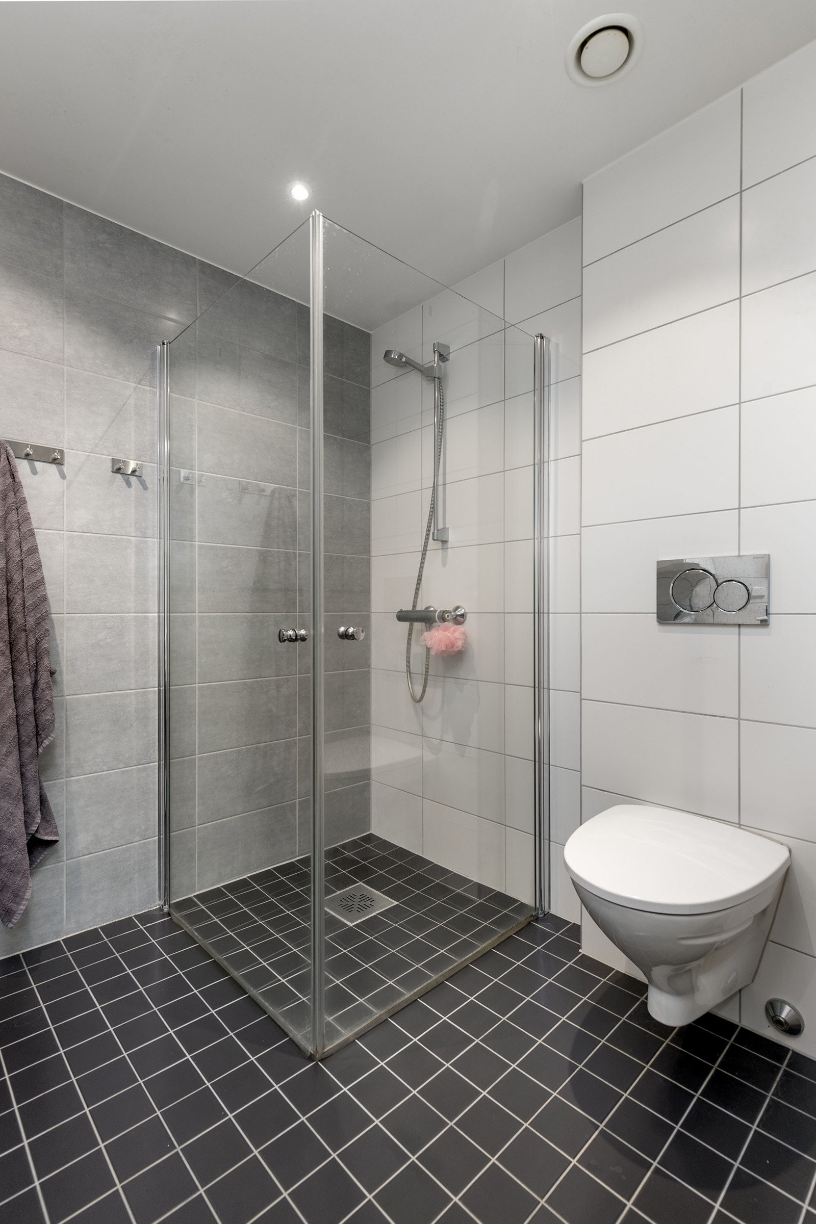 Dusj med innfellbare dører i herdet glass og veggfestet klosett med innebygget sisterne. Galleribilde