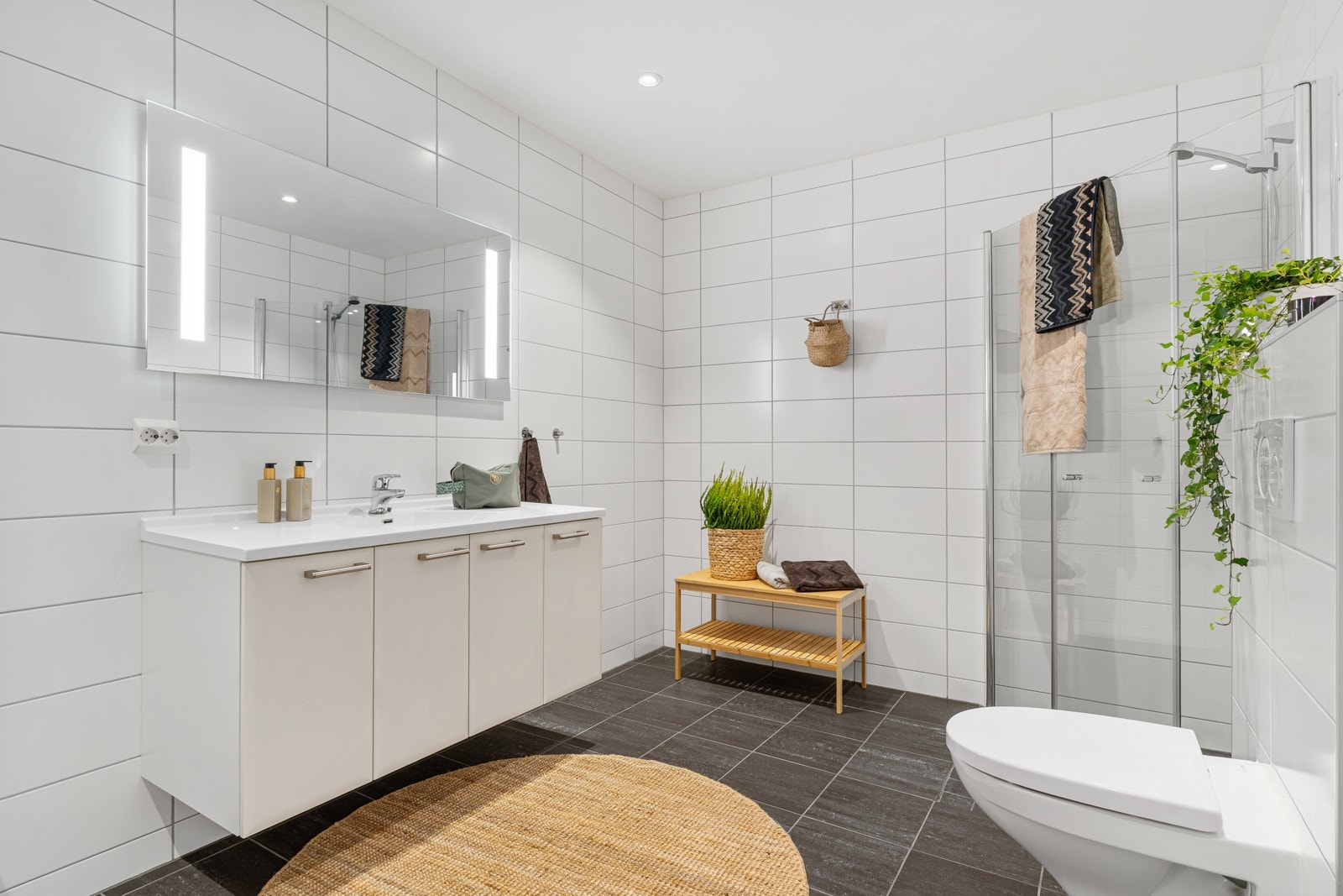 Her er det innredet med en stor skyvedørsgarderobe som har plass til både vaskmaskin og tørketrommel. Ellers er det innredet med servant og stort underskap, opplyst speil, toalett og dusjhjørne. Galleribilde