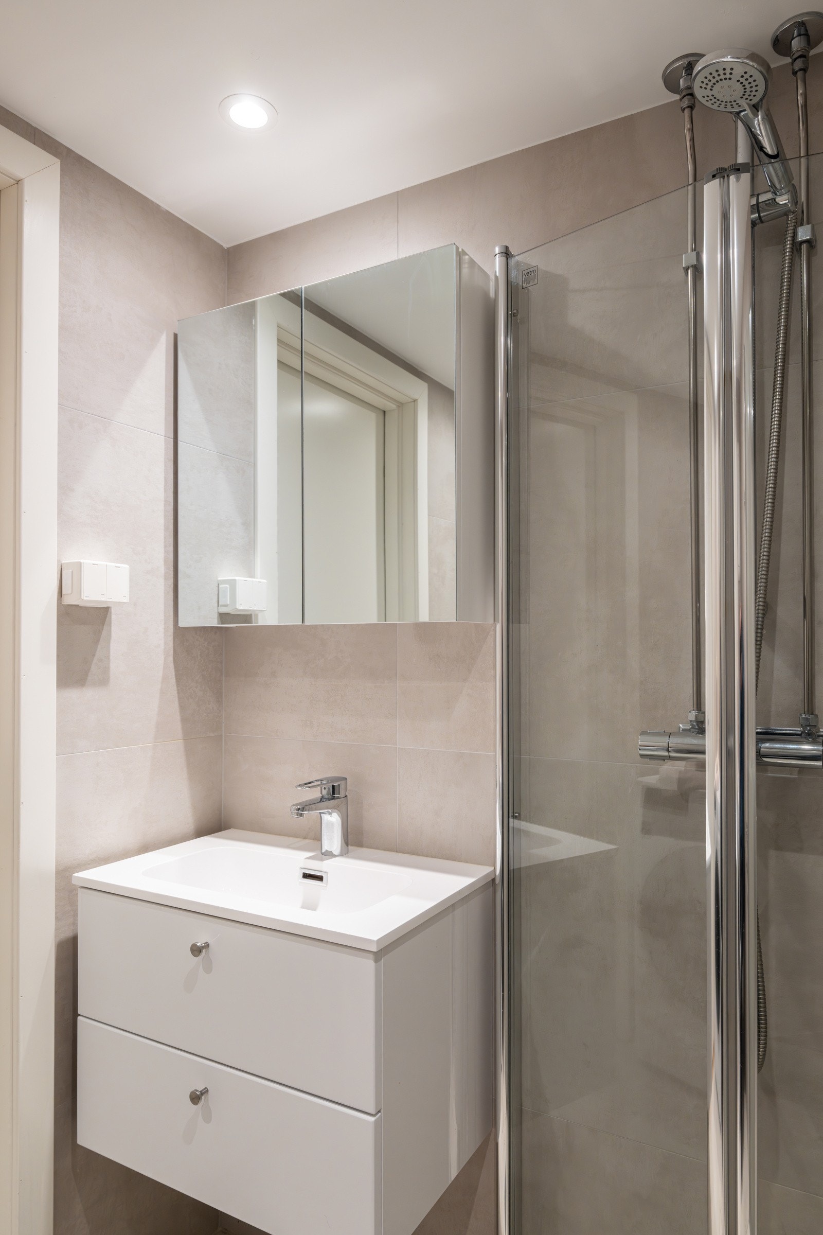 Lys baderomsinnredning med skuffer og heldekkende servant, vegghengt speilskap over. Galleribilde