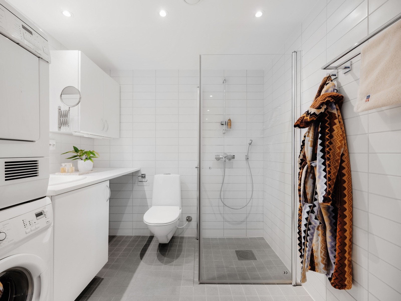 Badet er fra 2016 med flislagte gulv og vegger. Innredningen består av servant med underskap, overskap, speil, dusj med glassvegger og vegghengt toalett. Galleribilde