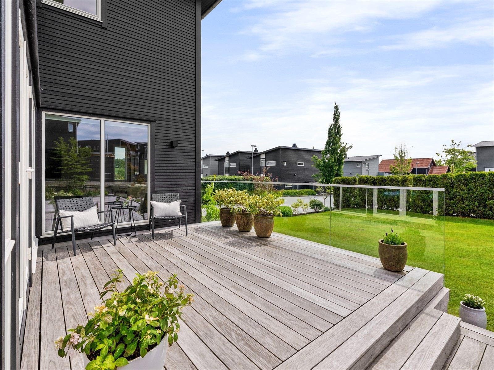 Kebony terrassen med glassrekkverk har utsikt til egen grønn oase, bestående av en romslig plen og flere plantede trær og busker. Hagen er praktisk, stelt og lett vedlikeholdt. Galleribilde