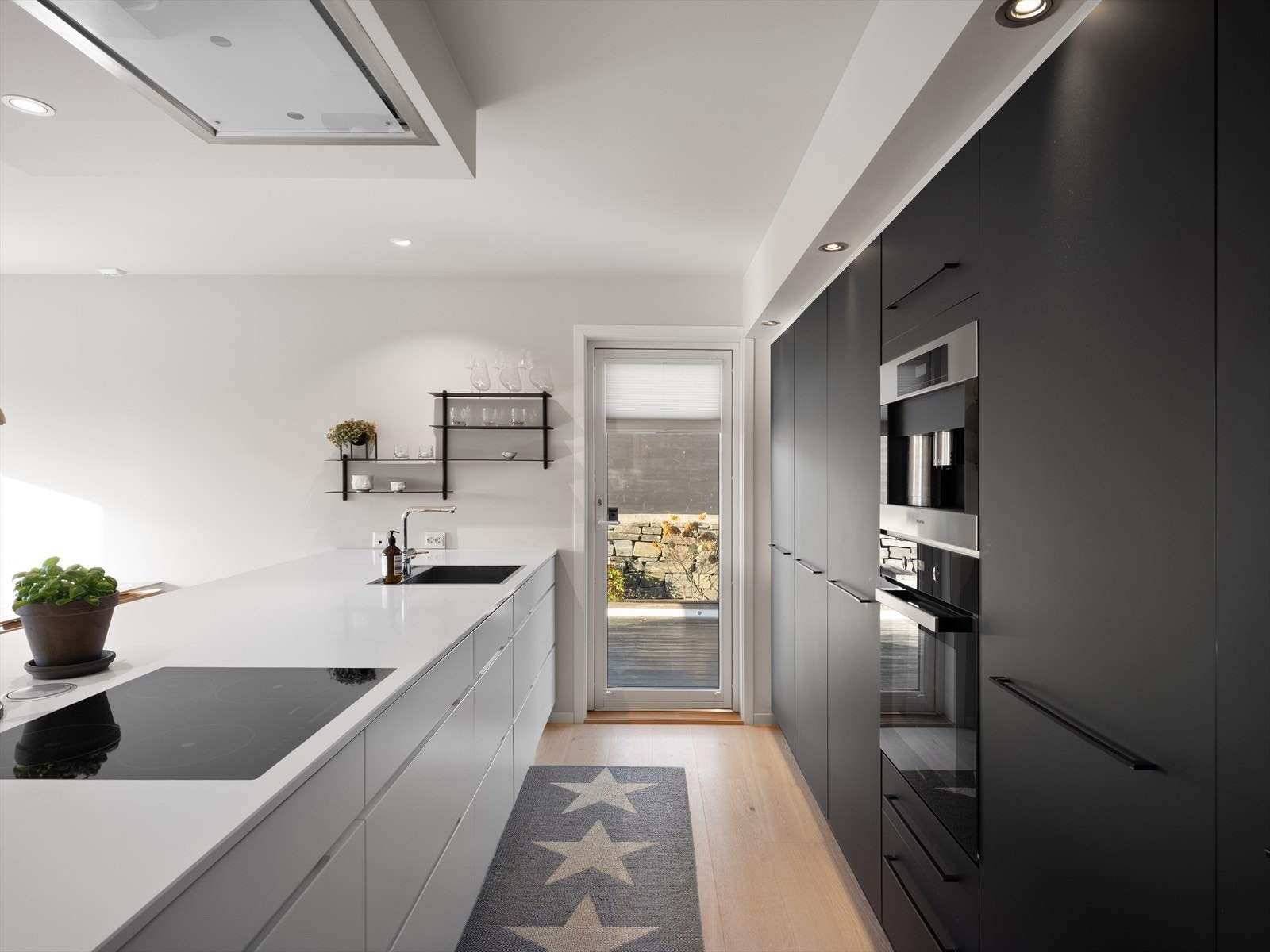 Pene kontraster mellom sorte høyskap og hvit kjøkkenøy. Benkeplate av Silestone, og Eiko distante ventilator over kjøkkenøy. Terrassedør i glass gir ekstra naturlig lys inn og rask kontakt for mat ute på fine dager. Galleribilde