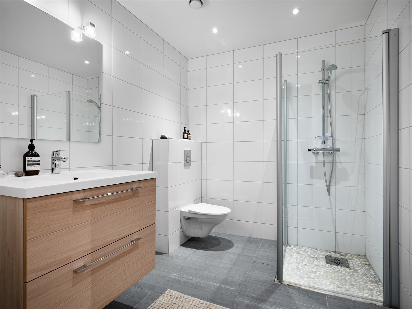 Delikat baderom også her, med tidløse kontraster mellom lyse fliser og skuffeseksjon i tre. Spotter i tak og dusjsone med rullestein. Galleribilde