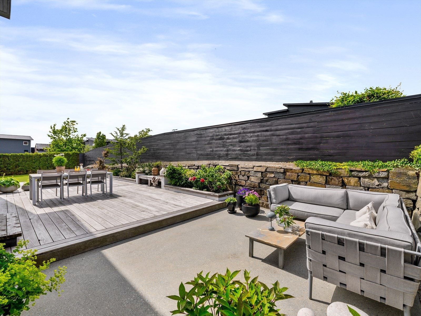 Vedlikeholdsfri, eksklusiv Kebony terrasse i pen kontrast til støpt platting og plen på hver sin side. Skjermede uterom med sol fra tidlig til sent og plass til samling i enhver anledning. Galleribilde