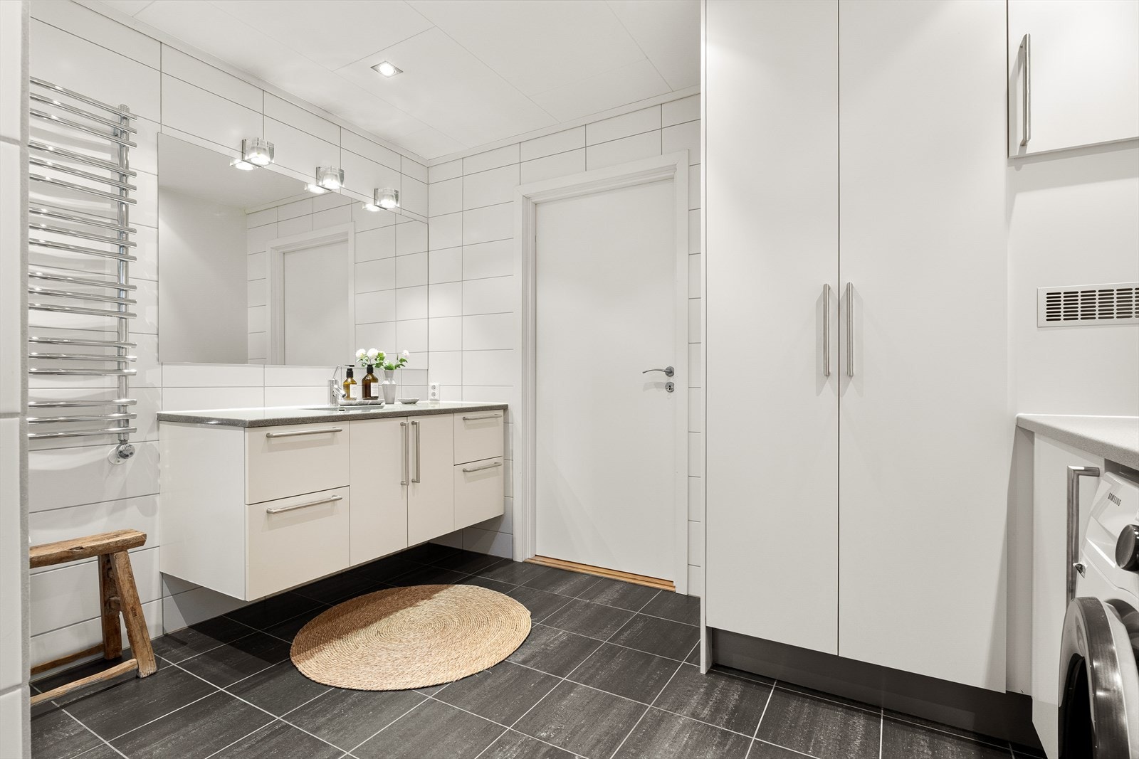 Rommet har varme i gulvet og er innredet med vegghengt servant, vegghengt toalett, dusjhjørne, håndkletørker og opplegg til vaskemaskin og tørketrommel. Galleribilde