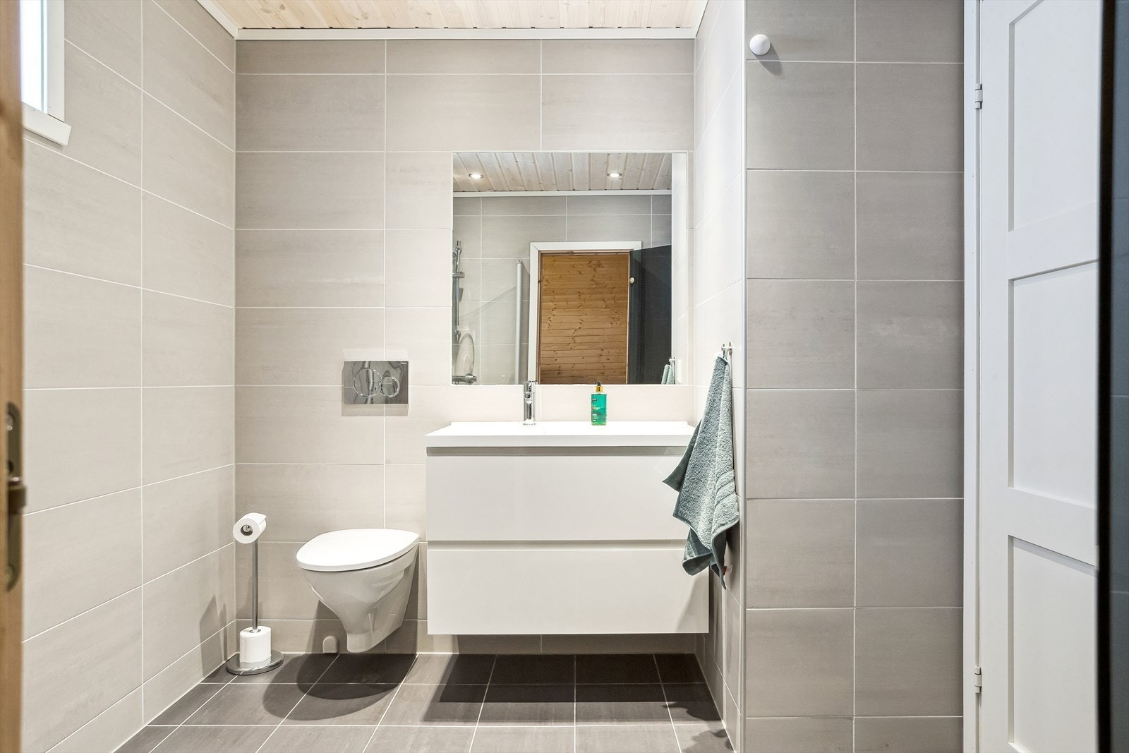 Helfliset baderom med vegghengt toalett, servant med skuffeseksjon samt et stort speil. Galleribilde