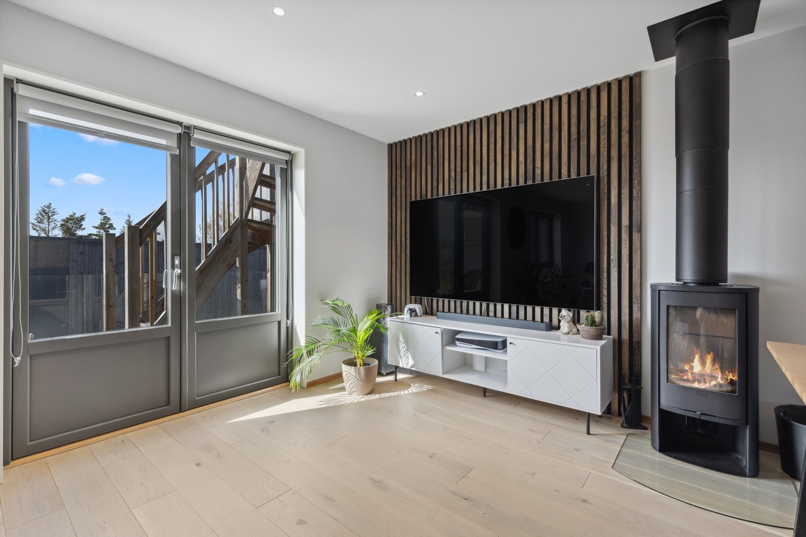 Den stilrene peisovnen varmer godt på kalde dager og gir en lun atmosfære til rommet. Himlingen er pent lyssatt med soneinndelte downlights. Legg merke til den flotte spileveggen i bakkant. Galleribilde