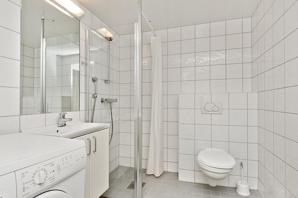 Flislagt bad med varme i gulv, dusj, servant med underskap, vegghengt wc og vaskemaskin Galleribilde