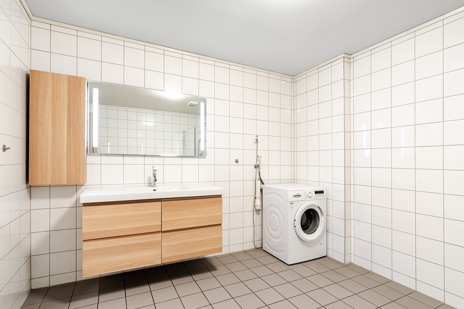 Lyst og romslig baderom med varme i gulv og romslig dusjnisje med innfellbare dusjdører, varme i gulv og opplegg til vaskemaskin. Galleribilde