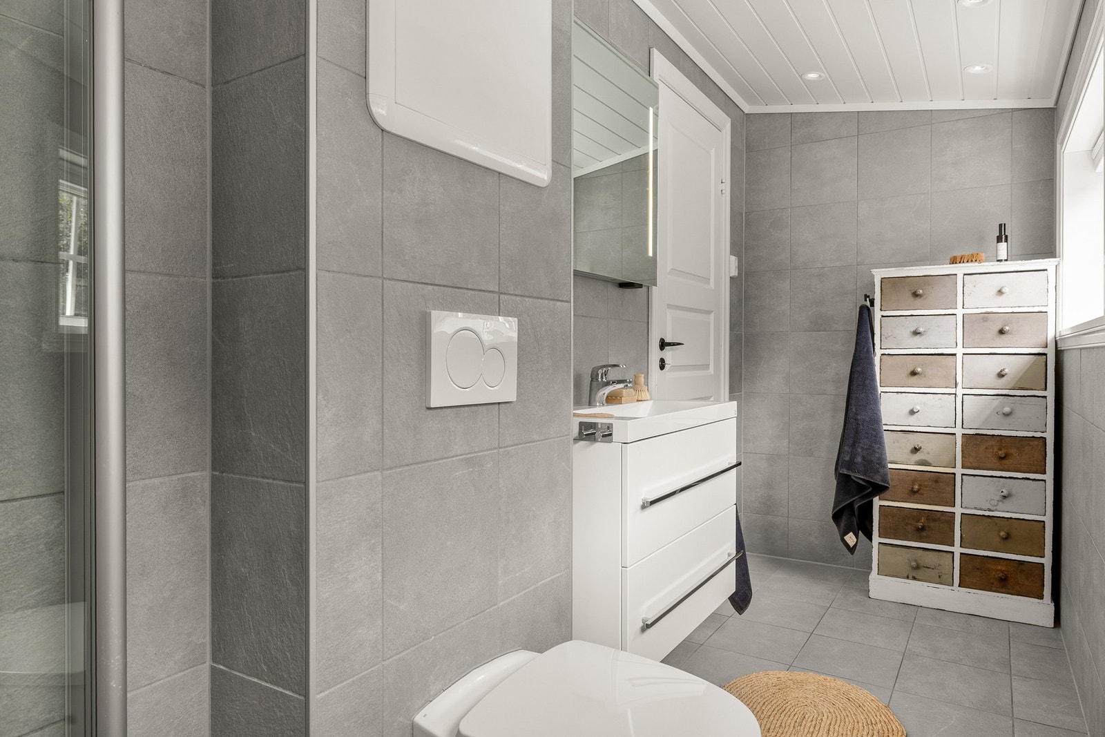 Det er innredet med vegghengt toalett, dusj med glassvegg og baderomsinnredning med servant, speil og belysning. Galleribilde