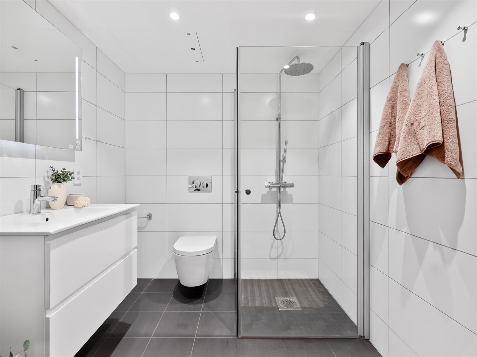 Baderom med servant, servantskap, speil, vegghengt toalett og dusj. Opplegg til vaskemaskin Galleribilde