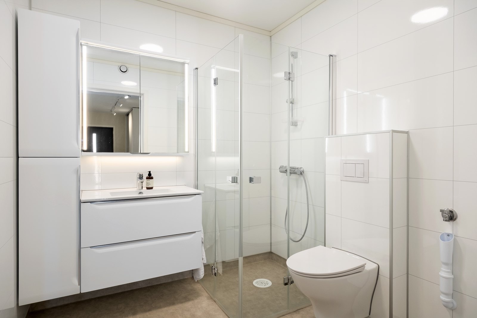 Lyst og romsleg bad som har innreiing med nedfelt servant, veggmontert toalett, romsleg dusj med dusjveggar og opplegg for vaskemaskin. Badet er oppgradert og har fått ekstra oppbevaringsmoglegheit. Galleribilde