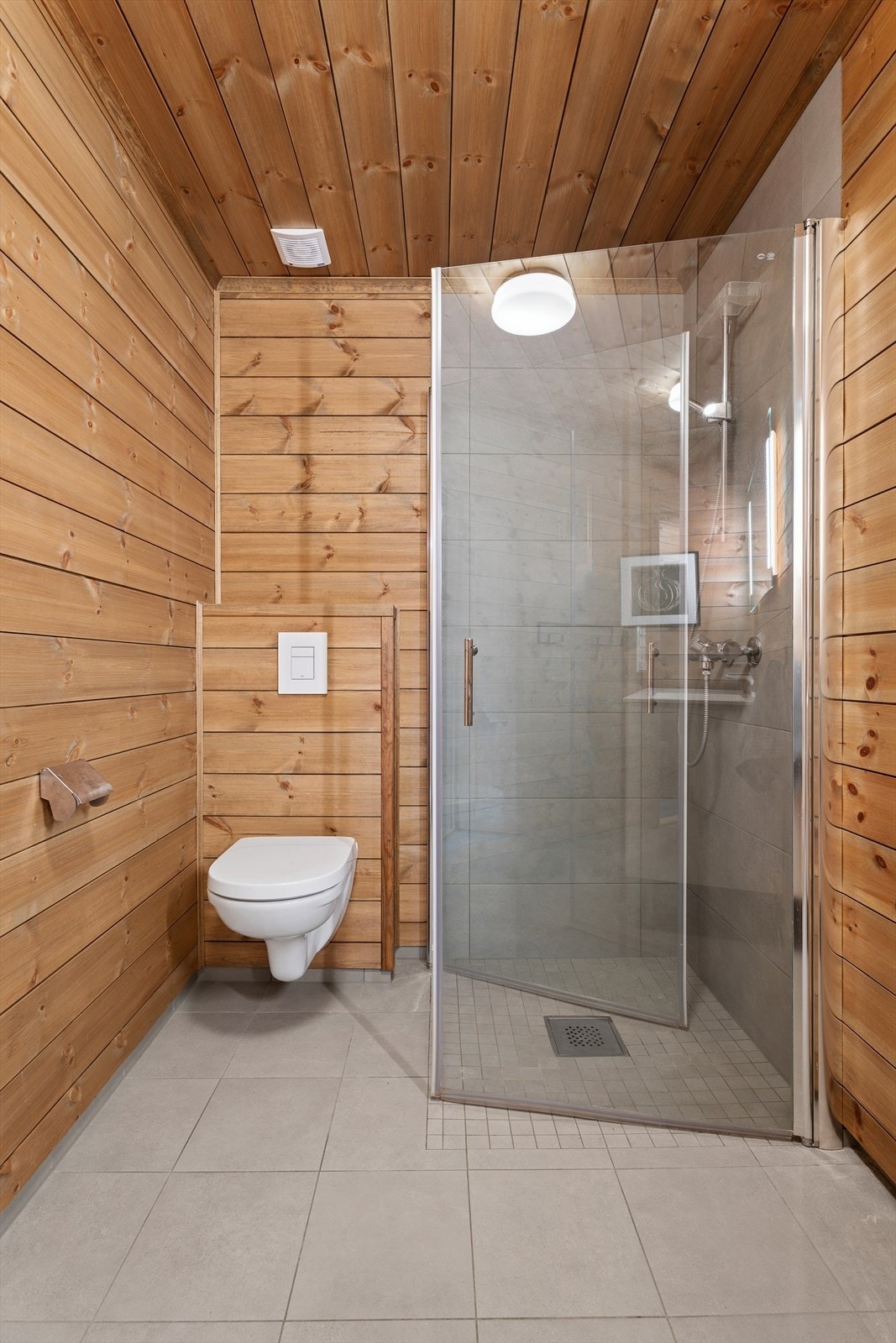 Rommet er innredet med vegghengt toalett, dusjhjørne med glassvegger, og servant med underskap. Galleribilde