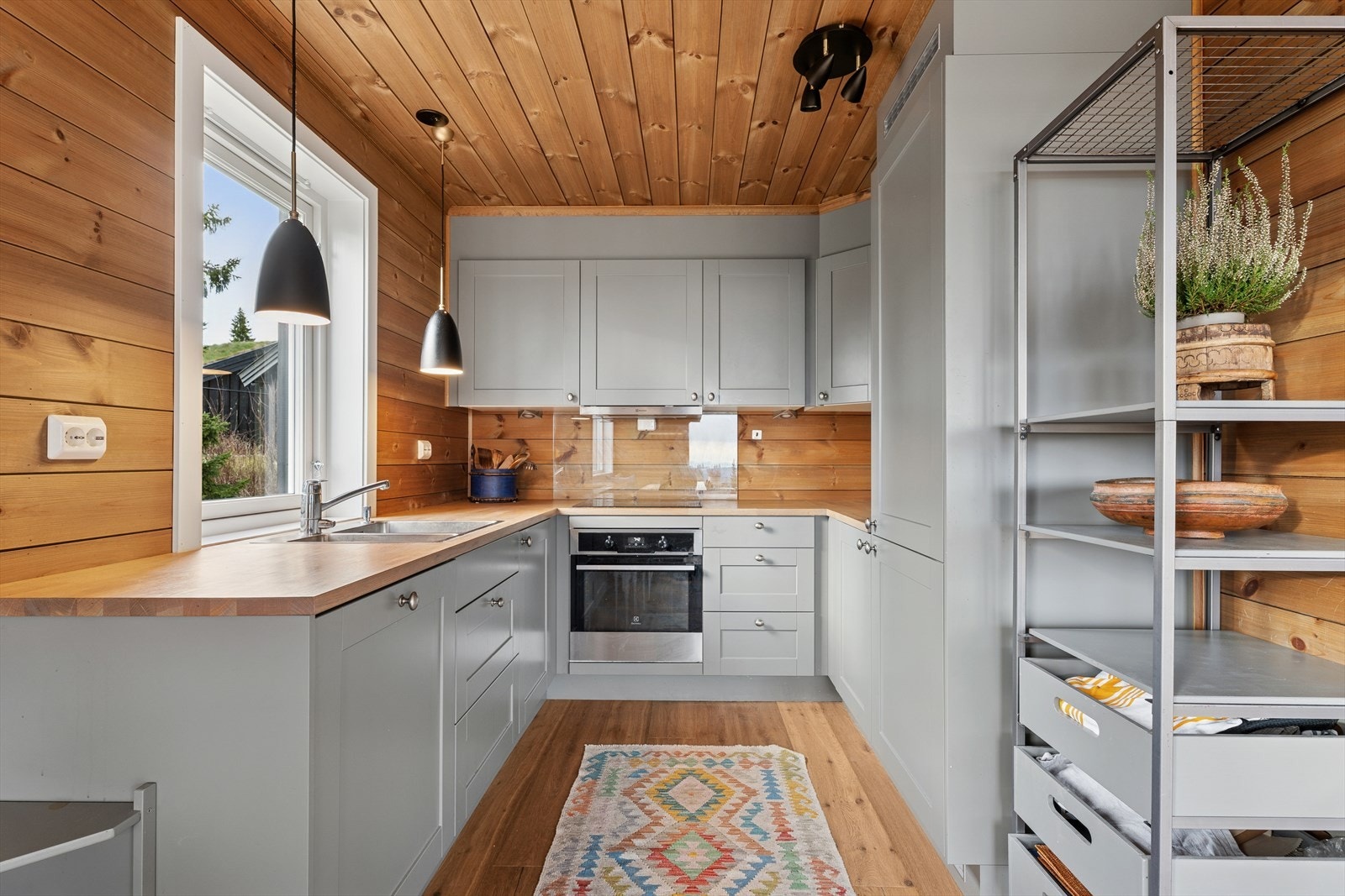 Kjøkkenet har en funksjonell innredning med laminerte skrog, profilerte fronter og heltre benkeplate med kjøkkenkum og kran. Over deler av benkeplaten er det montert glassfelt og belysning. Galleribilde