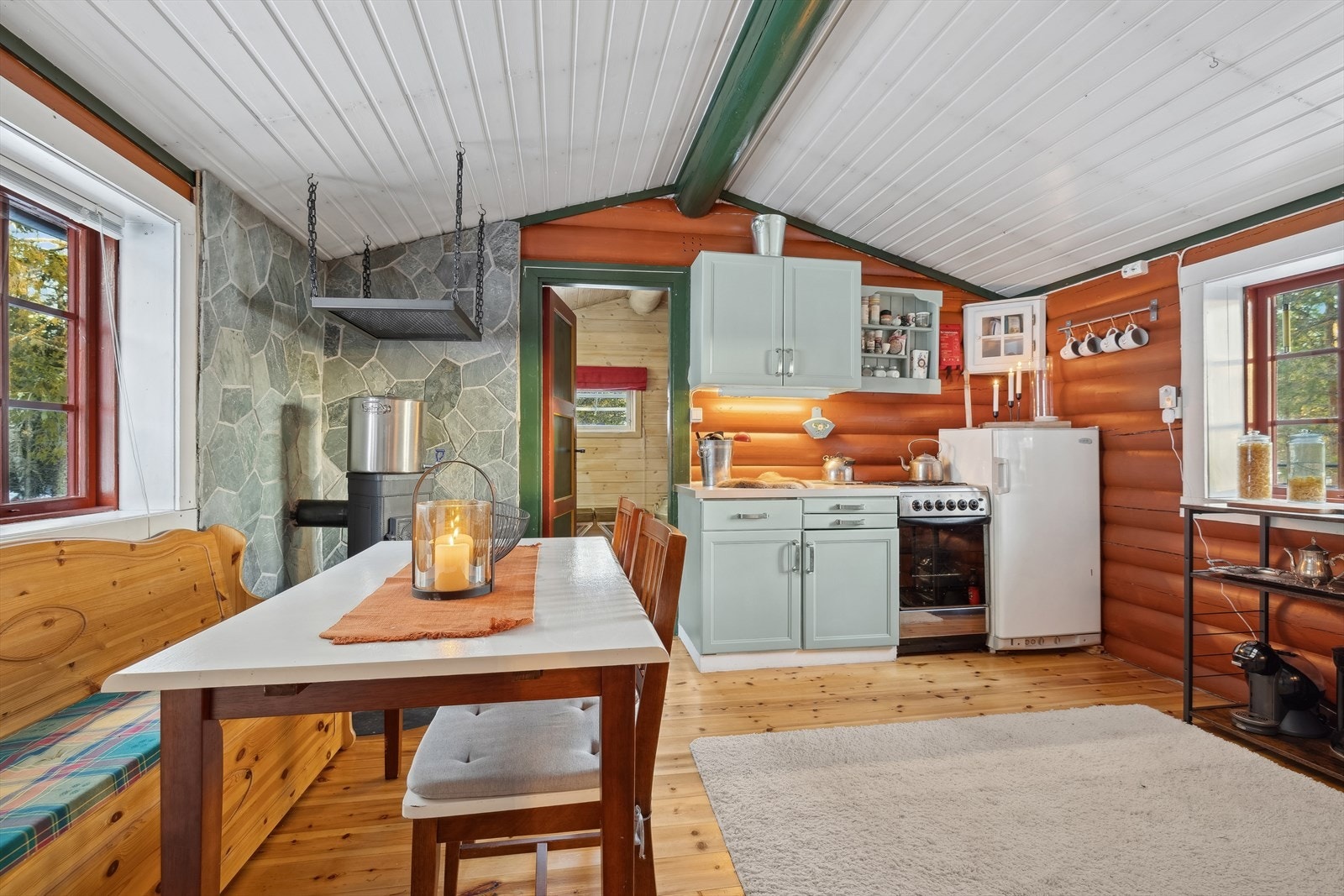 Todelt kjøkkeninnredning med eldre kostmalte overflater, det er ett-speils fronter på dører og skuffer med foliert benkeplate av stål. Galleribilde