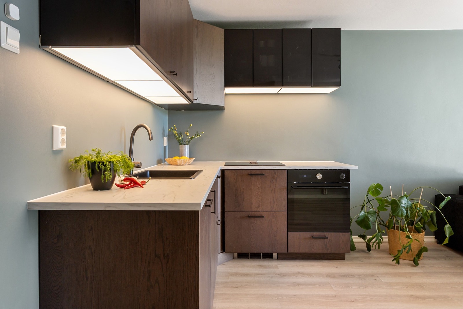 Lyse laminerte benkeplater, nedfeldt oppvaskkum i kompositt og sort ettgreps kjøkkenarmatur. Lys under overskap. Galleribilde