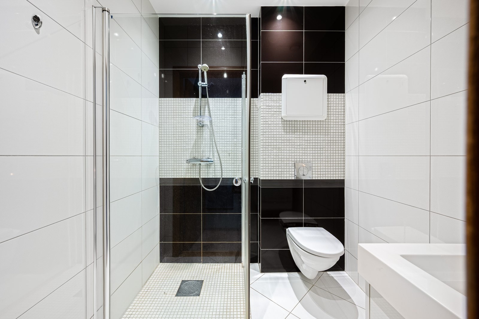 Badet er innredet med baderomsmøbel, heldekkende servant, speil med belysning, vegghengt toalett og dusj med innfellbare glassdører. Galleribilde