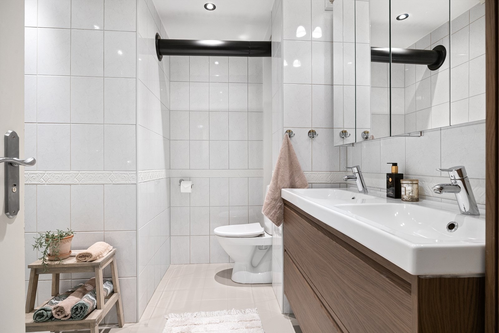 Badet fremstår som lyst og praktisk med flislagte gulv og vegger. Det er utstyrt med servantskap, toalett og dusjkabinett, samt mekanisk avtrekk som sikrer god ventilasjon og et behagelig inneklima. Galleribilde