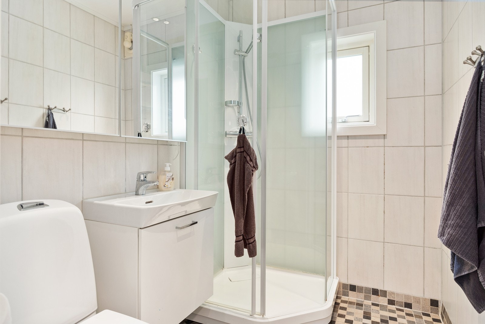 Tidløst flislagt baderom fra 2008 med varmekabler i gulv. Dusjkabinett og servantskap med blandebatteri og vask installert i 2018, og toalettet ble installert i 2021. Galleribilde