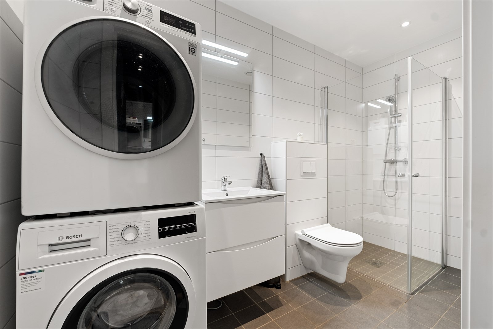 Dusjhjørne med glassdører, opplegg for vaskemaskin og vegghengt toalett. Galleribilde