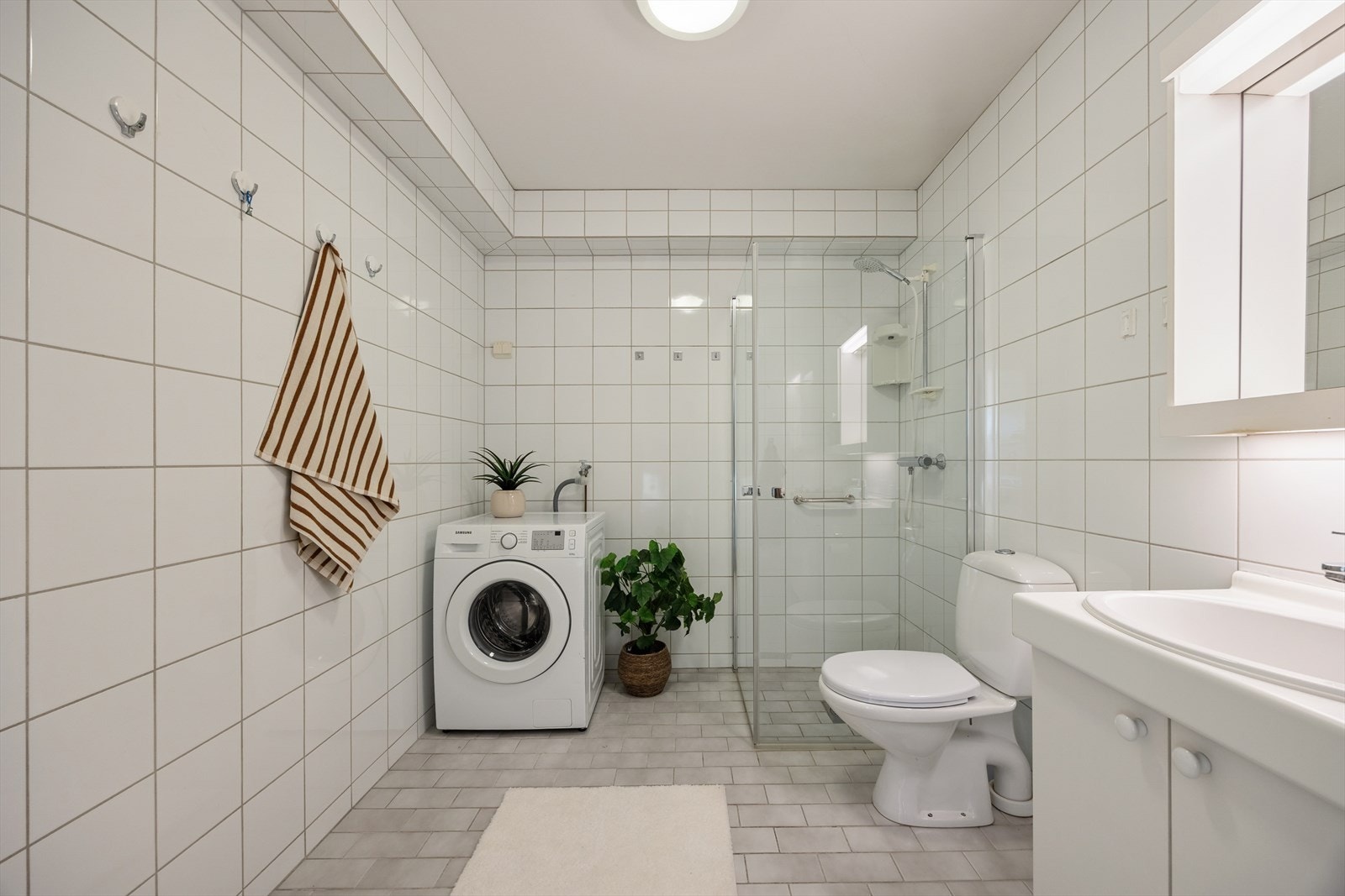 Badet er flislagt og fremstår som funksjonelt og lettstelt. Det er innredet med servant med nedfelt vask, toalett og hjørnedusj, samt opplegg for vaskemaskin som gir en praktisk og effektiv løsning i hverdagen. Galleribilde