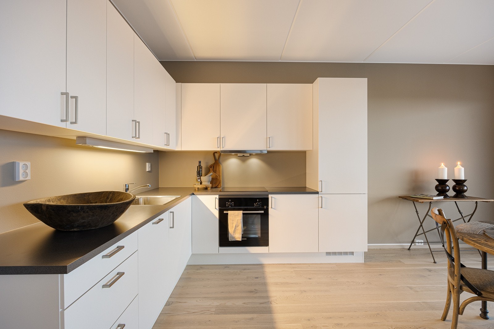 Kjøkkeninnredningen er fra Sigdal og har glatte, hvite fronter og laminat benkeplate. Hvitevarer inkluderer stekeovn, platetopp, oppvaskmaskin og kombinert kjøle/fryseskap. Galleribilde