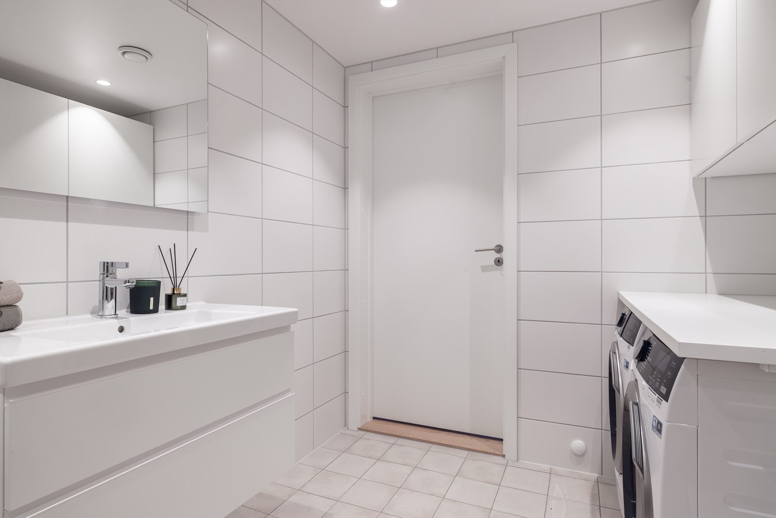 Videre finner du servant på hvit skuffeseksjon med speil, veggmontert toalett og dusjhjørne med innfellbare glassdører. Galleribilde