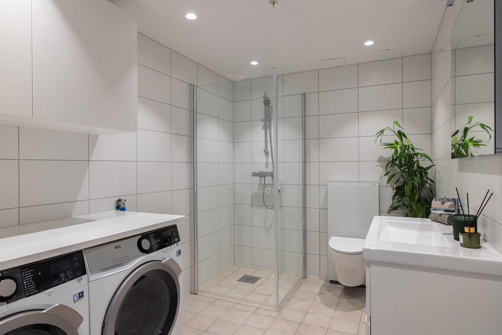 Romslig bad i tilknytning til entréen, kombinert med vaskerom. Det er vannbåren gulvvarme, hvite fliser på veggene og downlights i himlingen. Galleribilde