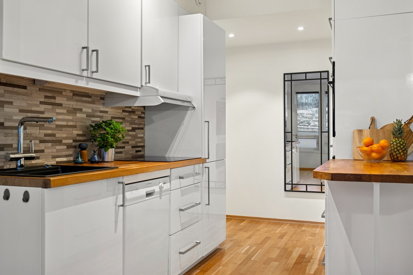 Innredningen er stilrent med hvite glatte fronter, benkeplate i heltre og fliser på vegg over benk Galleribilde