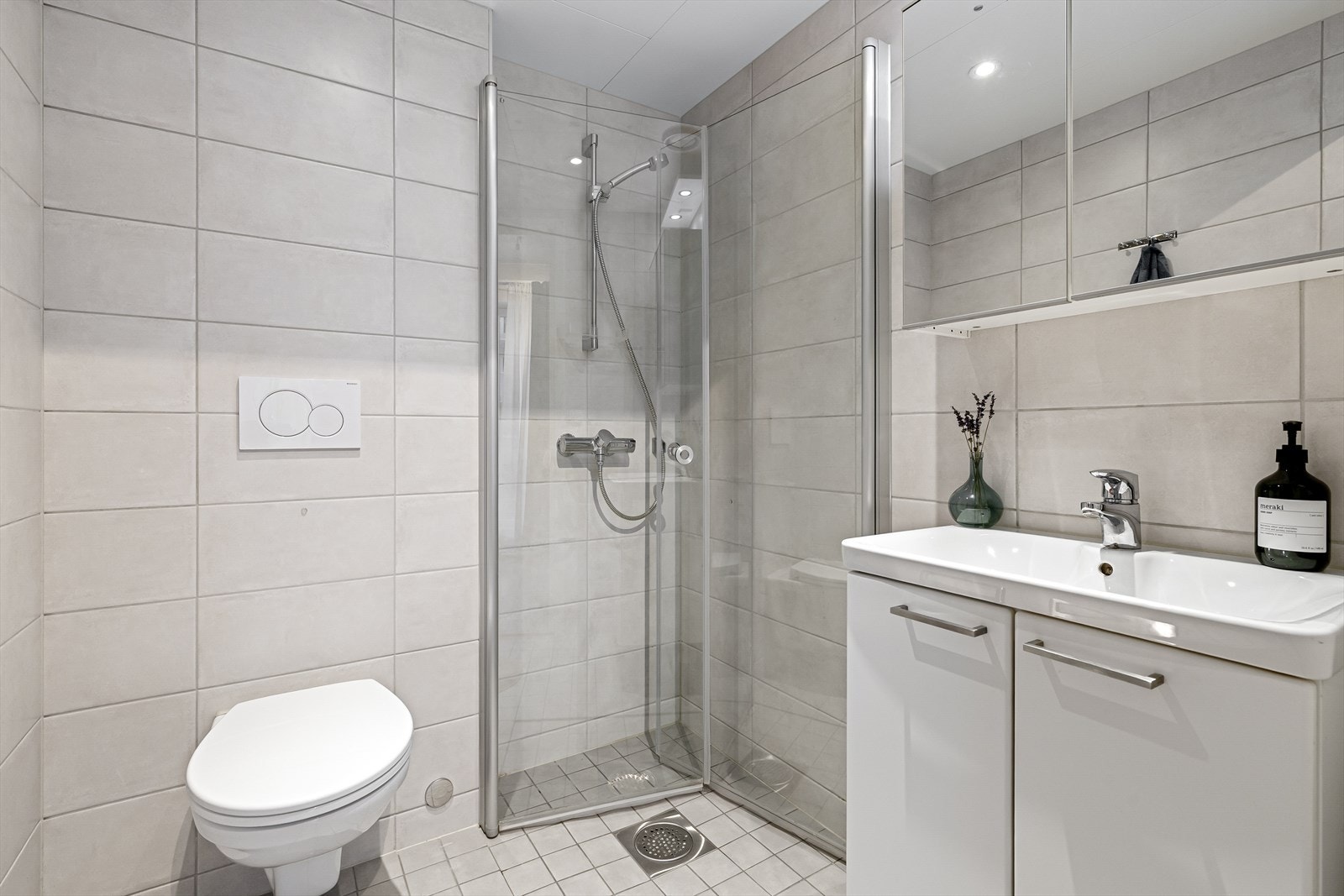 Pent flislagt bad med varmekabler i gulv. Praktisk oppbevaringsplass i speilskap og baderomsinnredning. Badet er også utstyrt med vegghengt toalett og dusjhjørne med innfellbare glassdører. Galleribilde