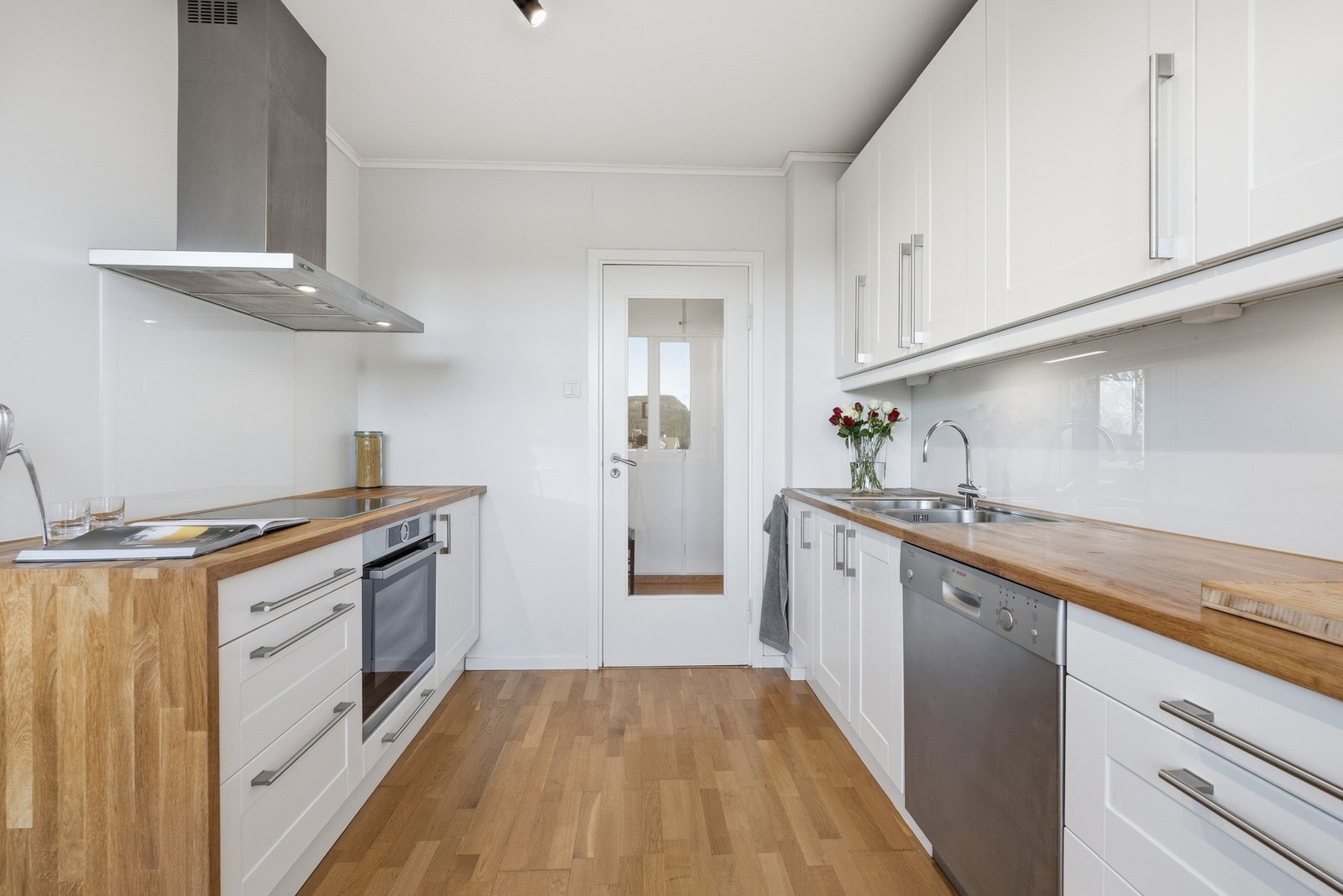 Hvit kjøkkeninnredning med profilerte fronter og heltre benkeplate. Det er integrert koketopp og stekeovn Galleribilde