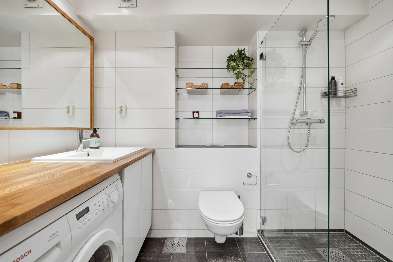 Badet har flislagt gulv, vegghengt servant og opplegg for vaskemaskin Galleribilde