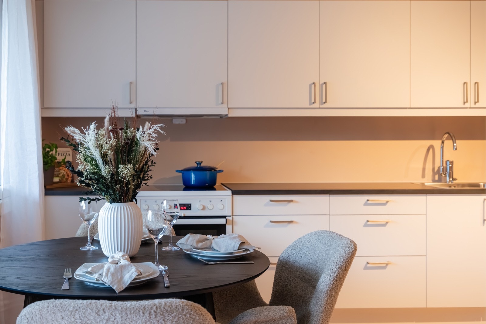 Kjøkkeninnredning fra 2024 med lyse slette fronter, benkeplate av kompaktlaminat, nedfelt oppvaskkum, i tillegg til benkeskapsbelysning (2025) og stikkontakter under overskap. Galleribilde