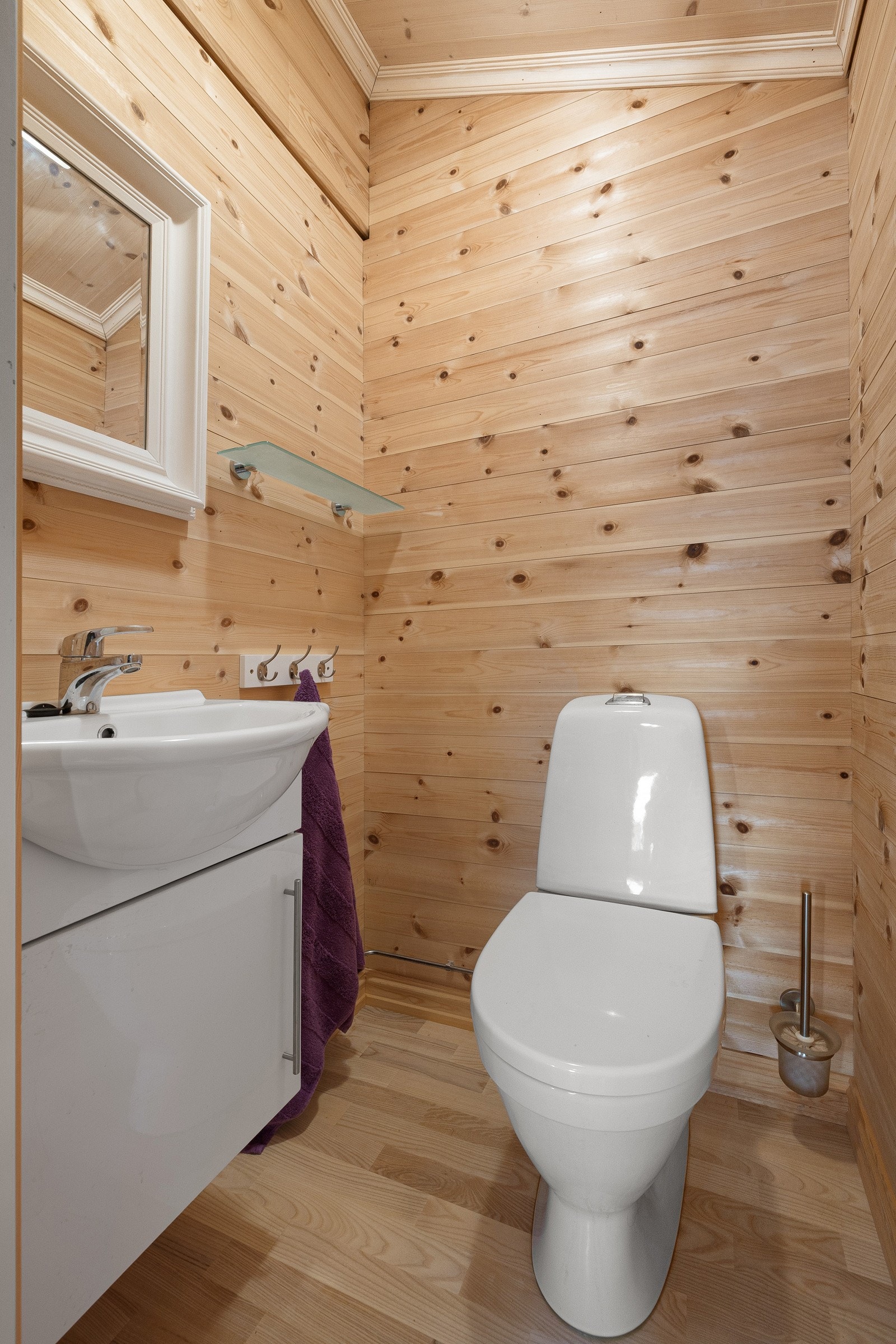 Toalettrom med parkett på gulv samt trepanel på vegger og i himling. Rommet er innredet med gulvmontert toalett og servant i baderomsinnredning med speil. Galleribilde