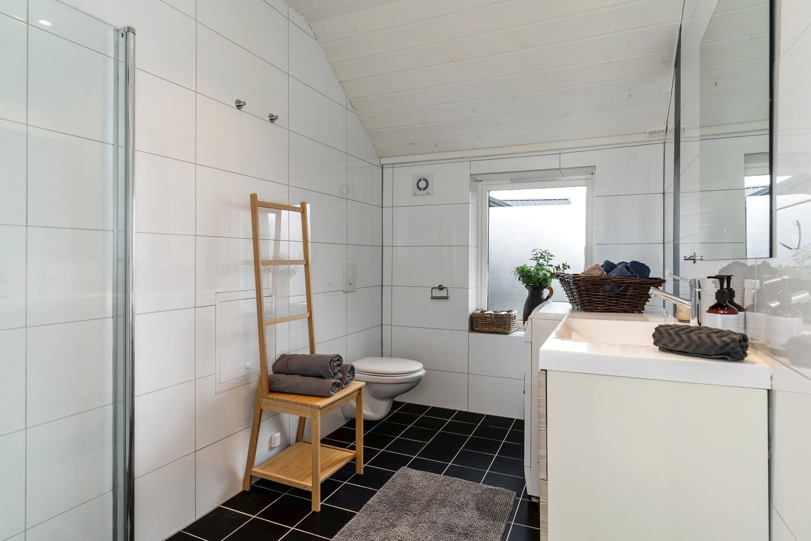 Delikat, flislagt bad innredet med servantskap med skuffer, dusjvegger og vegghengt toalett. Galleribilde