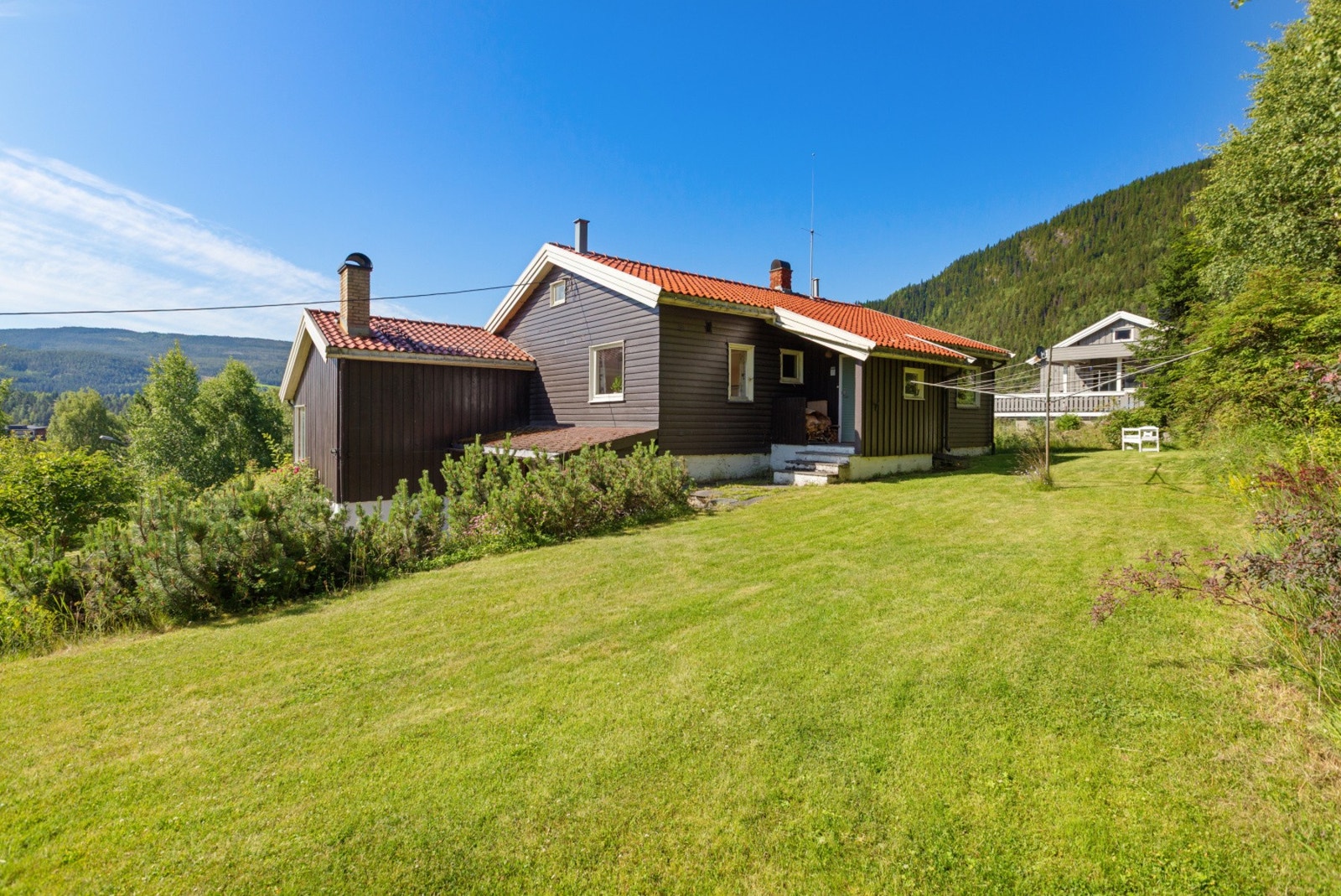 Romslig, pent opparbeidet tomt med plen og beplantning, ellers naturtomt i skrående terreng. Galleribilde