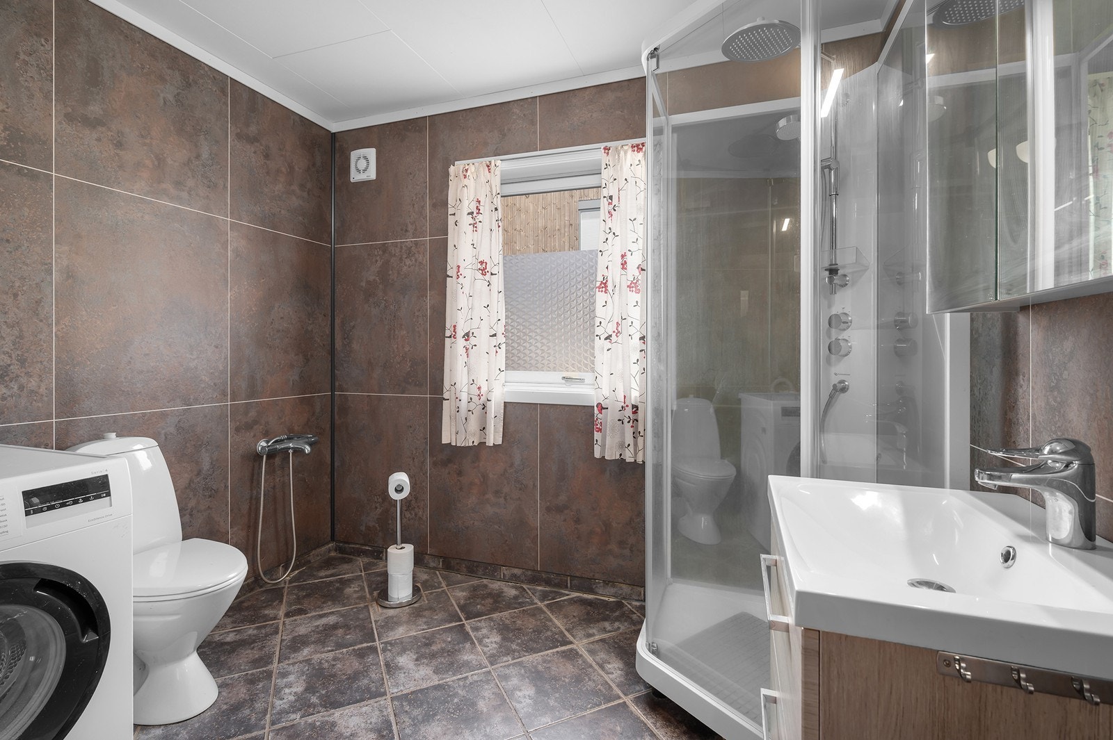 Delikat bad med fliser i 1 etasje. Dusjkabinett og god plass til vaskemaskin. Baderomsplater på vegger montert 2023. Galleribilde