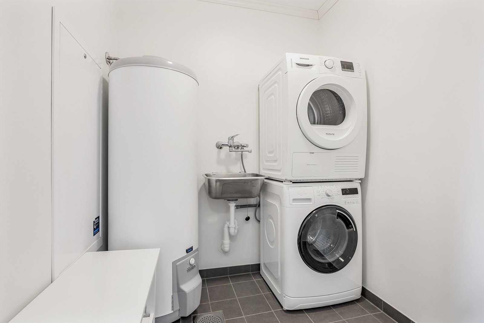 Praktisk og funksjonelt vaskerom innredet med skyllekum og opplegg og plass for vaskemaskin og tørketrommel. Galleribilde