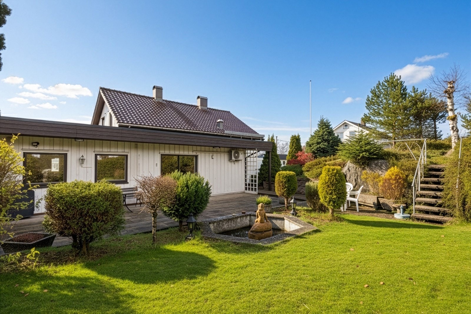 Velstelt hage med skifersteinsbelagt terrasse og betongveranda. Galleribilde