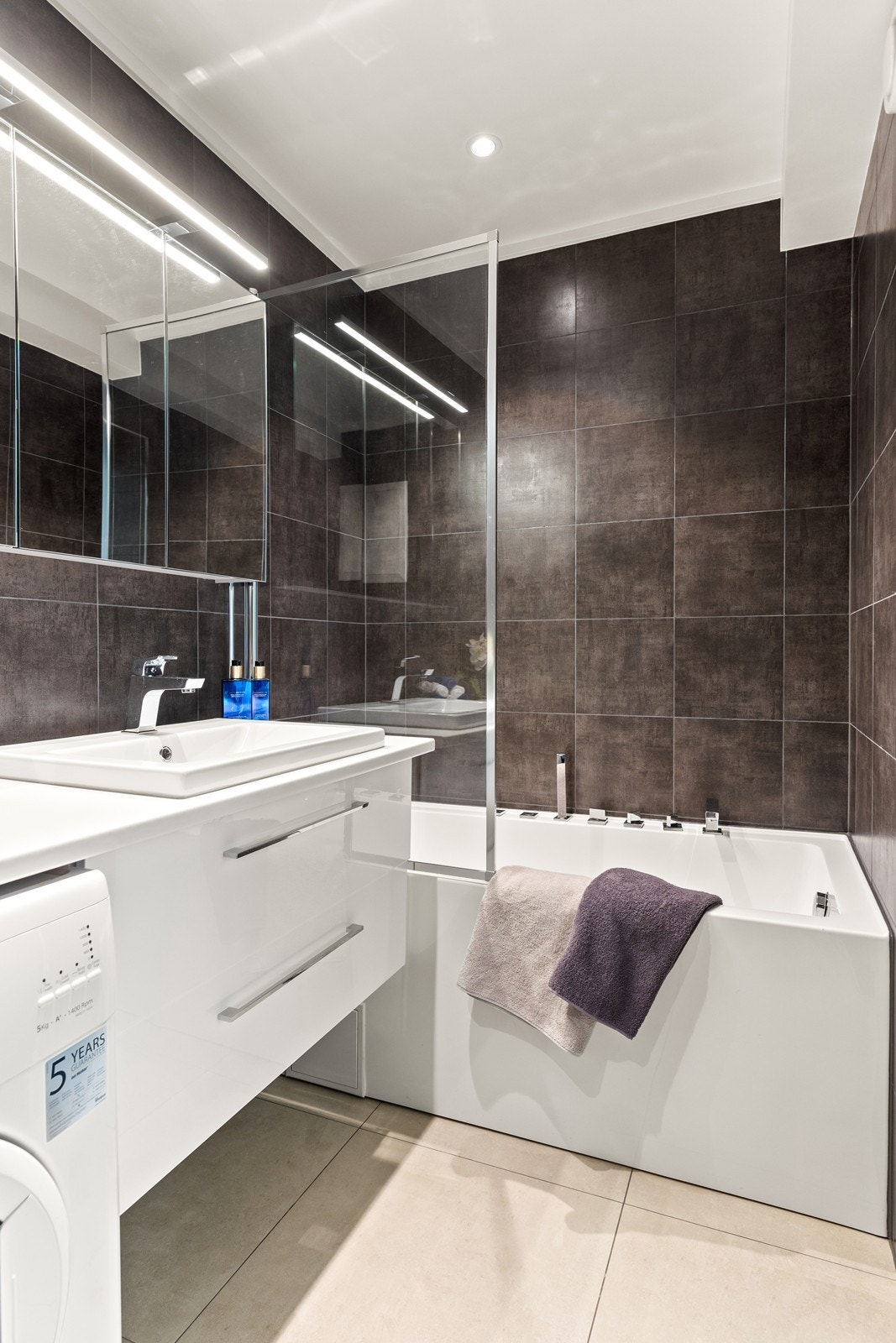 Badet har underliggende varmekabler og har badekar med praktisk dusjvegg i glass Galleribilde