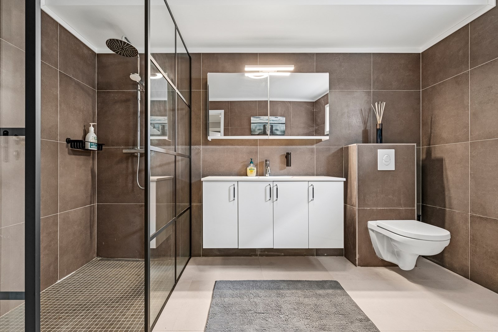 Badet har moderne store fliser på gulv og vegger - Her finner du vegghengt toalett, dusjnisje m/glassvegger, hjørnebadekar og baderomsinnredning Galleribilde