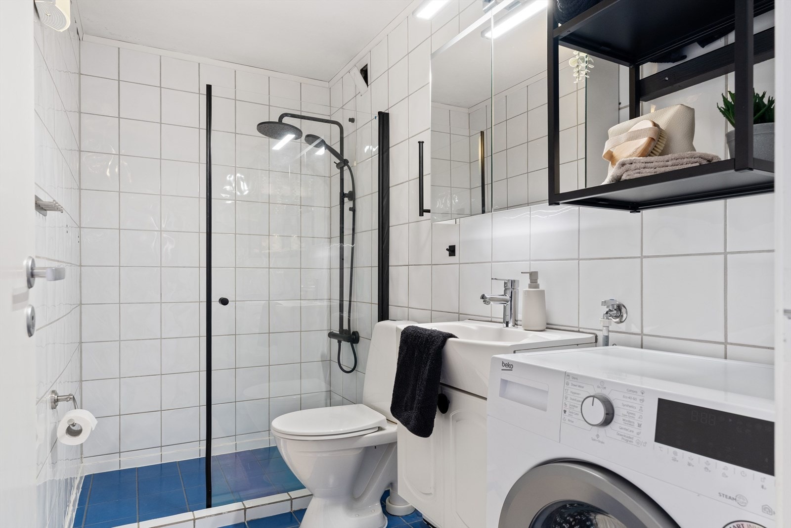 Flislagt bad utstyrt med dusjhjørne, servant og opplegg for vaskemaskin. Galleribilde