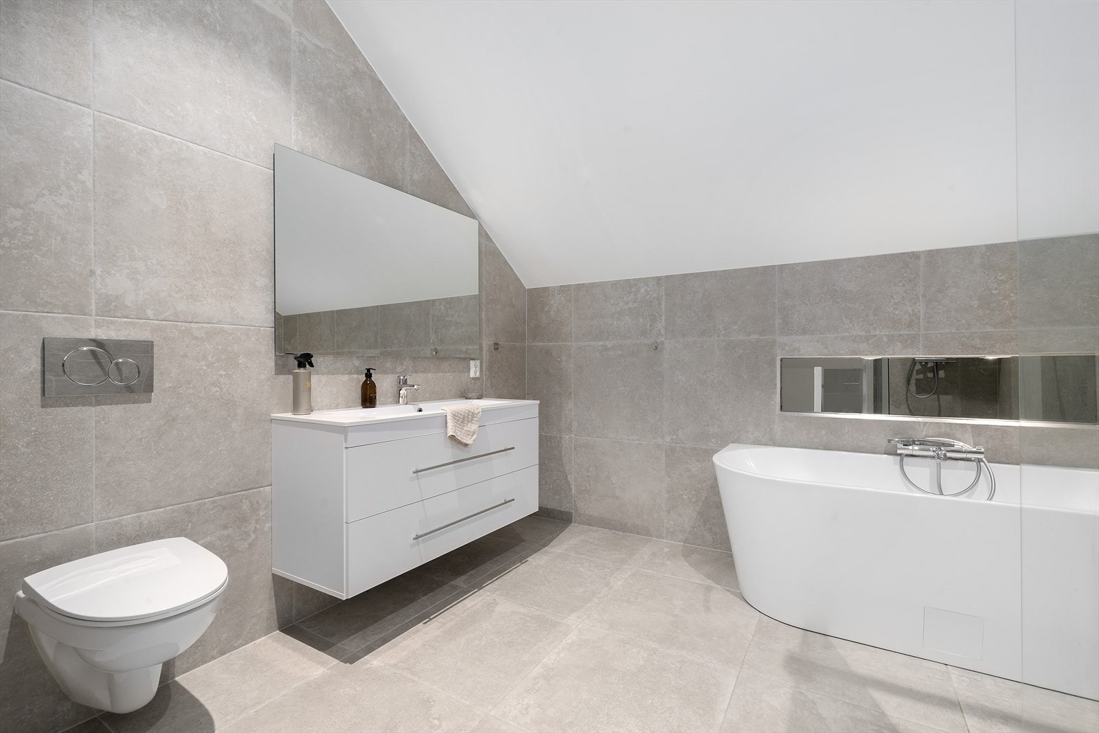 Badet er pent flislagt og mosaikkfliser i dusjsone. Innredet med en delikat servantinnredning med nedfeltservant, dusjhjørne, badekar og toalett. Galleribilde