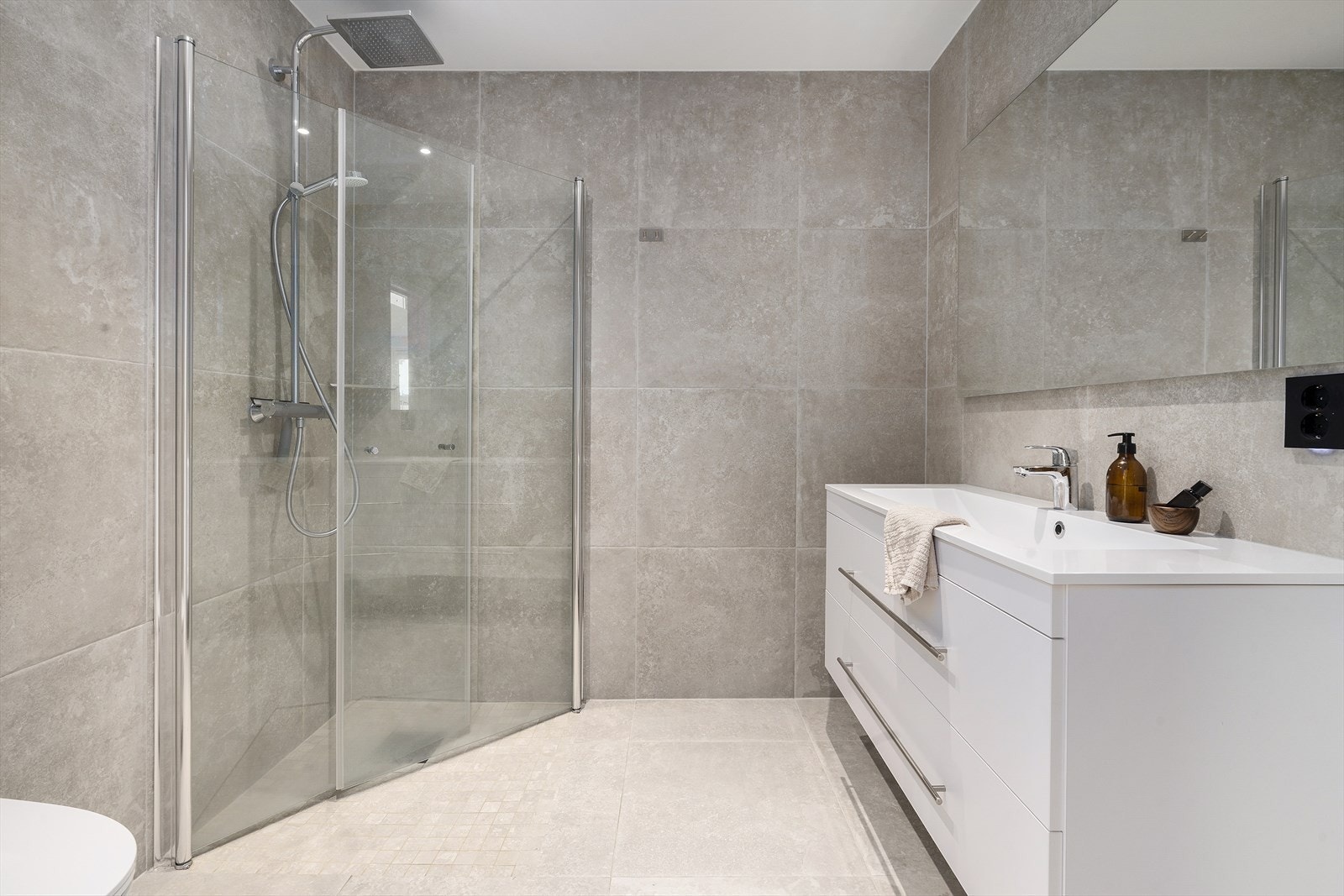 Badet i 2.etasje er lekkert, med moderne farge- og materialvalg. Baderomsinnredning i hvit utførelse med heldekkende nedfelt servant, rom for oppbevaring og speil. Videre har badet vegghengt toalett og dusjnisje med regndusjarmatur. Galleribilde