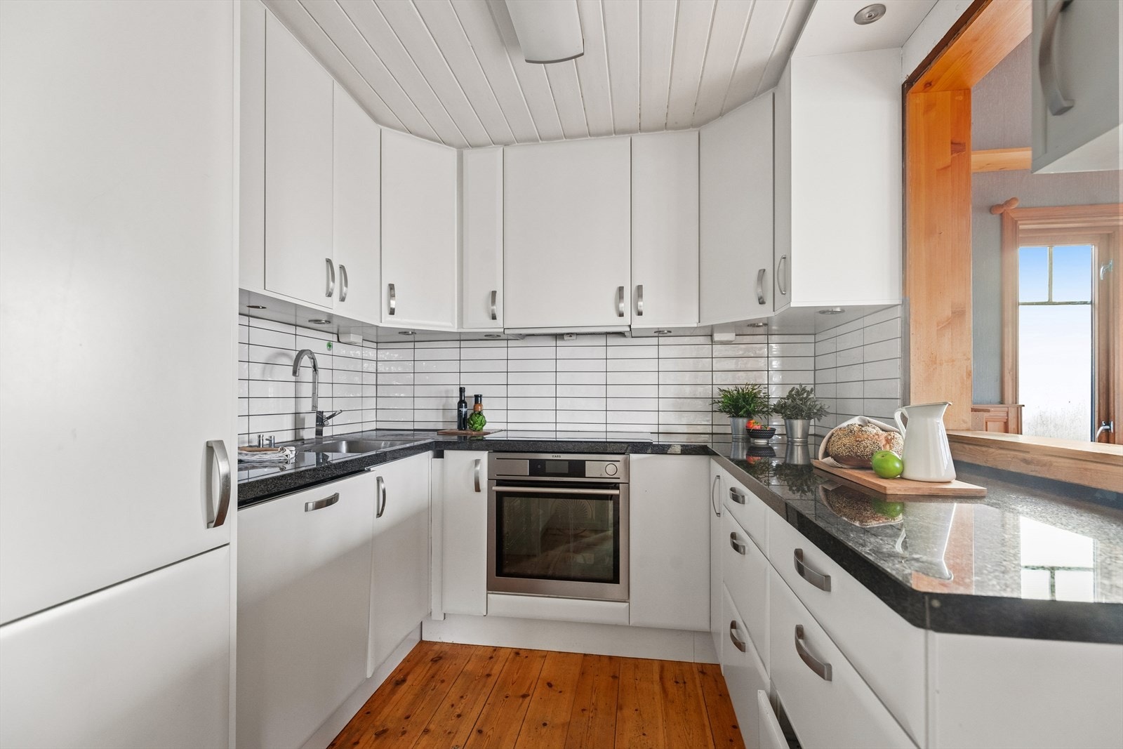 Kjøkken er utstyrt med hvit glatt kjøkkeninnredning, stein benkeplate, fliser over benk, utslagsvask med blandebatteri, kjøkkenventilator og opplegg for oppvaskmaskin. Lys under overskap. Kjøkkeninnredning og hvitevarer med ukjent alder. Galleribilde