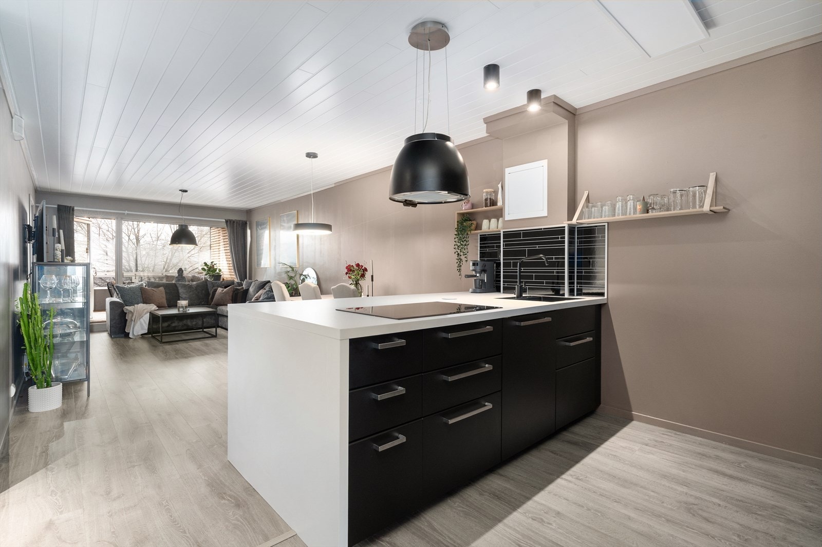 Beskyttelsesplater i flisimitasjon på vegg over laminat benkeplate med god arbeidsflate, nedfelt induksjonstopp og oppvaskkum i lakkert stål. Galleribilde