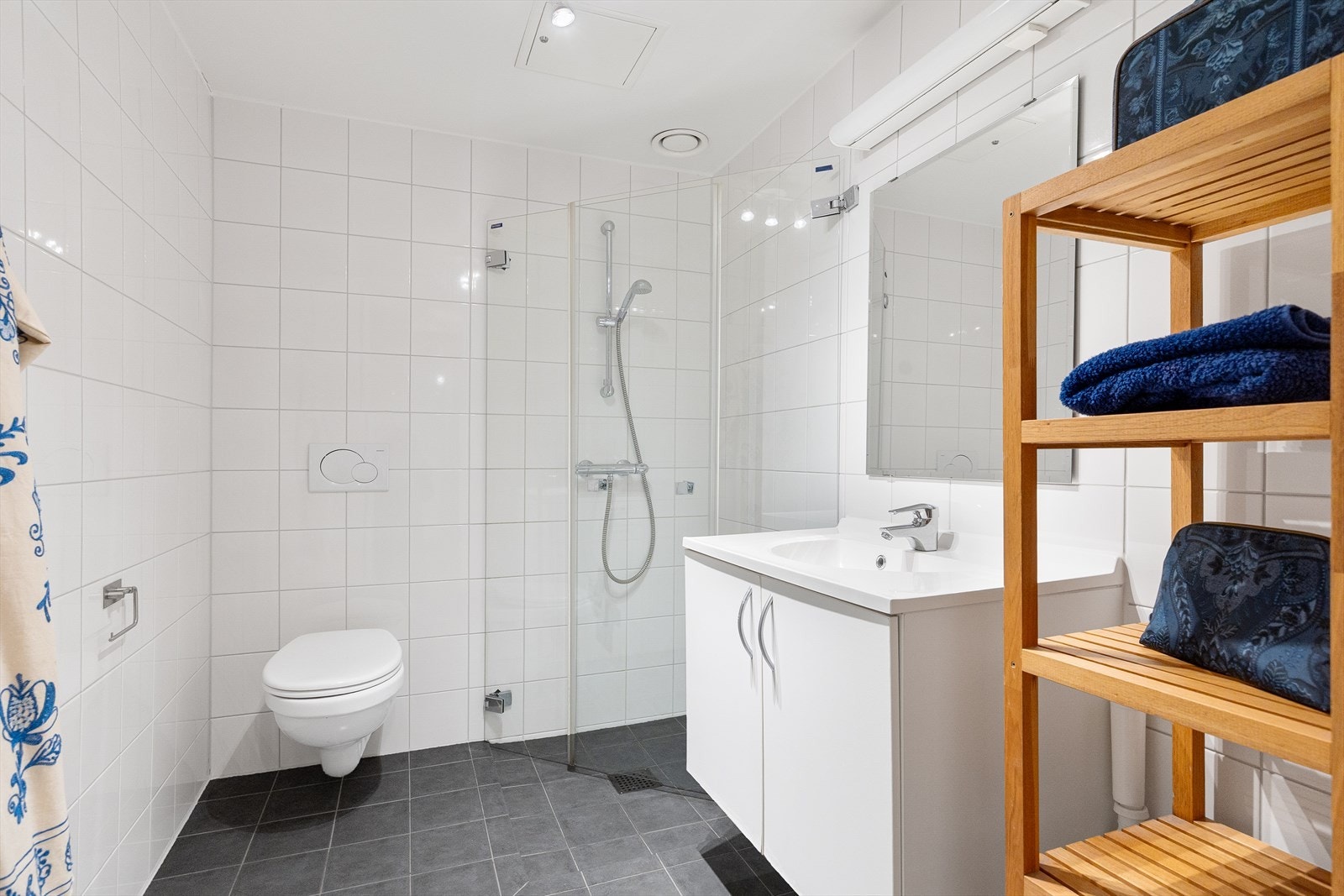 Badet er innredet med veggmontert toalett, dusjhjørne med vegg/dør i herdet glass samt servant med skap, speil og belysning. Galleribilde