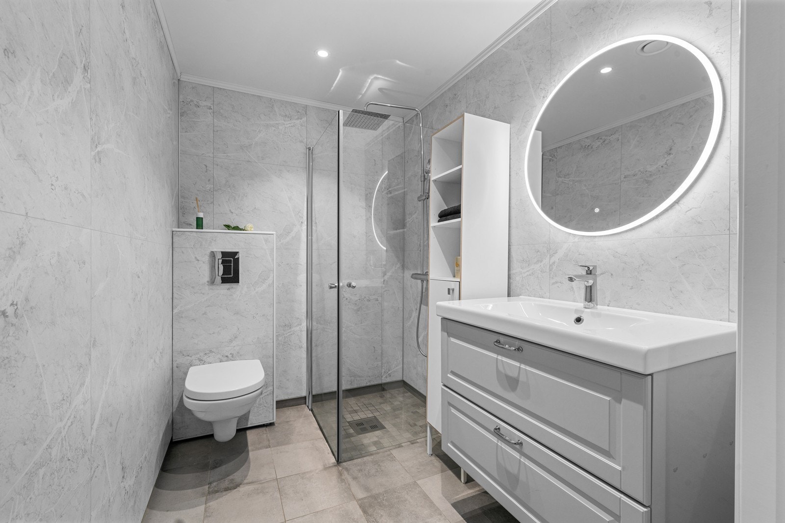 Pent flislagt baderom innredet med helservant på skuffeseksjon, vegghengt toalett og regnfallsdusj. Galleribilde