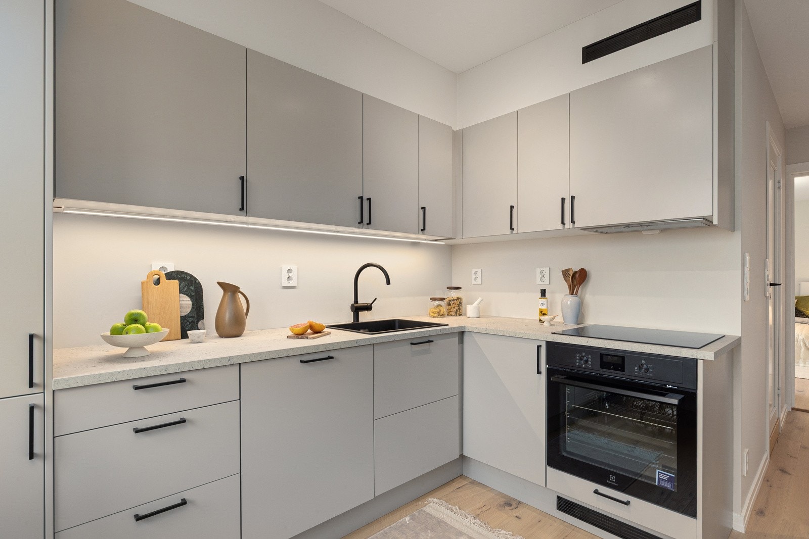 Innredningen har moderne glatte fronter og laminert benkeplate med nedfelt sort oppvaskkum. Praktisk med belysning under overskapene. Galleribilde